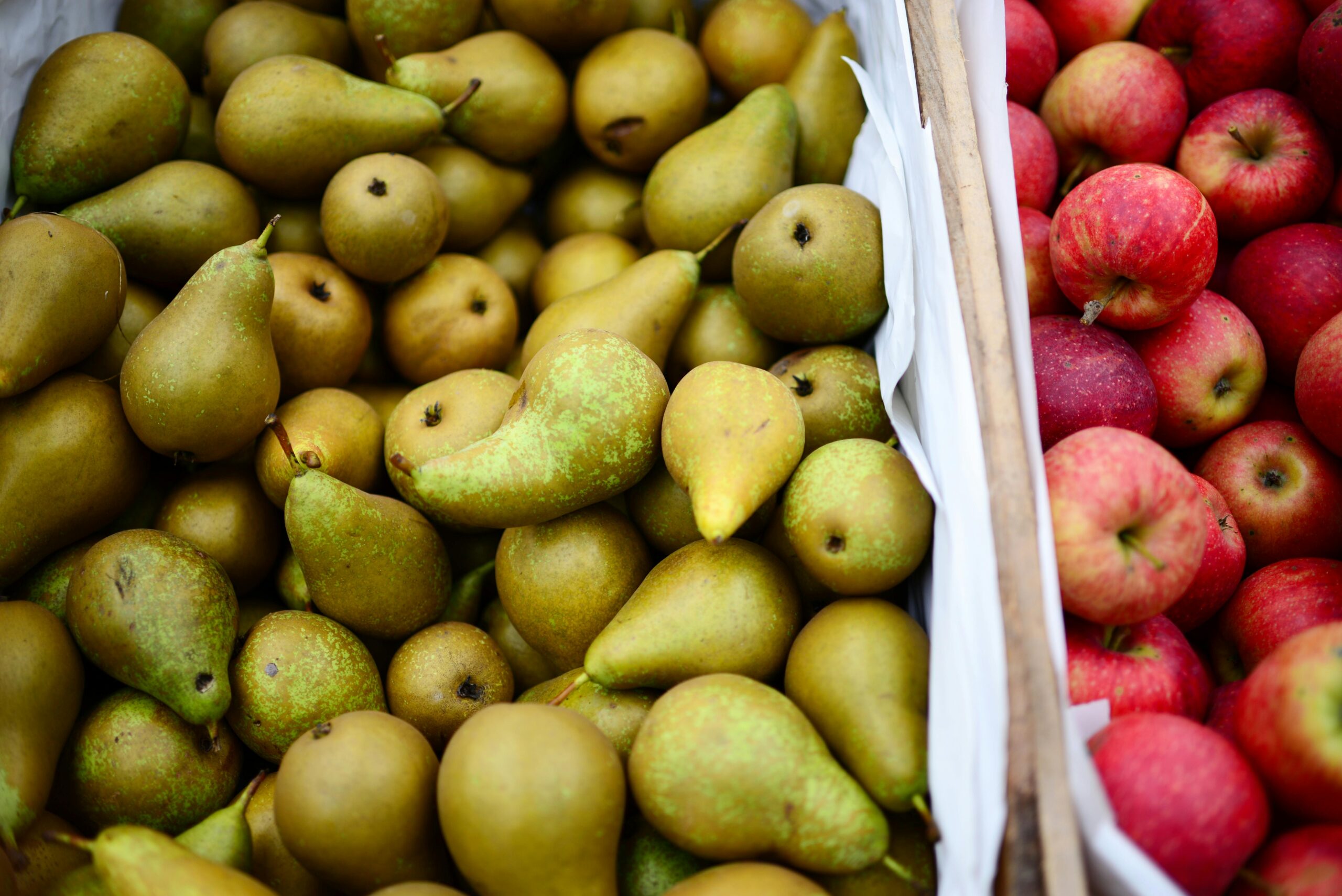 a crate that holds bright green pears. next to a crate that is holding apples
